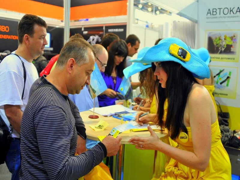 Девушка промоутер в необычной шляпе и желтом фирменном платье