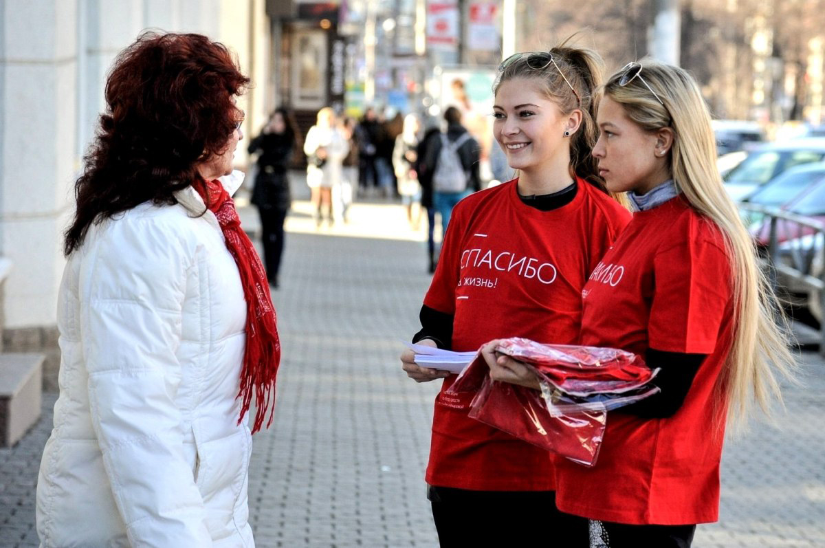 Промоутеры в красных футболках раздают рекламные материалы